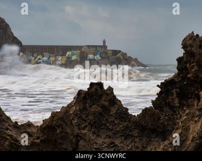Stormy sea waves crashing on rocky pier - A dramatic, long exposure shot of powerful ocean waves crashing against a pier with colorful breakwater bloc Stock Photo