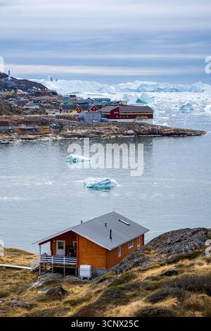 Scenic view of Ilulissat, Greenland, showcasing colorful houses and large icebergs floating in Disko Bay. The serene summer setting captures the beaut Stock Photo