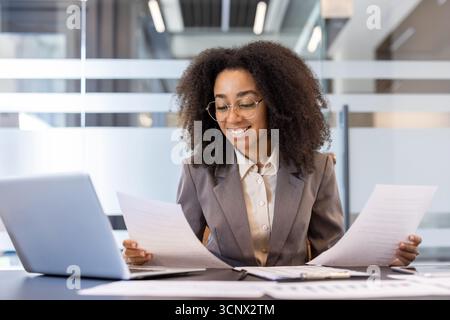 African-American young businesswoman lawyer working in office, sitting at table with laptop and studying documents. Stock Photo