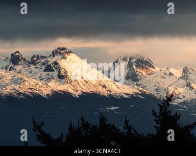 Majestic snow-capped Patagonian mountains bask in the golden glow of sunset, creating a stunning contrast with the dark foreground and dramatic cloudy Stock Photo