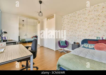 A stylish and inviting bedroom showcasing a comfortable bed, desk, and modern decor, illuminated by natural light through large windows Stock Photo