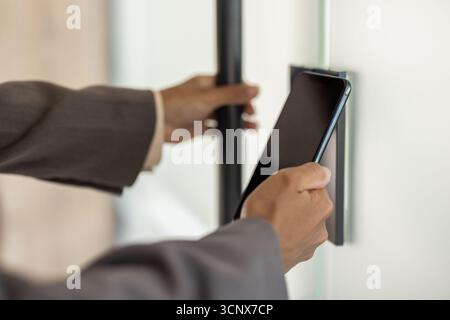 Close-up photo of the hands of a young African-American woman in a suit opening an office door by scanning a mobile phone. Stock Photo