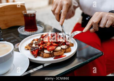A person enjoys a delicious plate of waffles topped with fresh fruit and drizzled with chocolate in a cozy cafe setting, capturing a moment of sweet i Stock Photo
