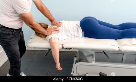 Cropped unrecognizable physiotherapist man assisting an anonymous woman lying on a treatment table during a rehabilitation session in a clinic for the Stock Photo