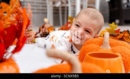 A delightful 4 month old baby boy smiling among cozy Halloween decorations, with bright orange pumpkins plush toys and autumn leaves, capturing the wa Stock Photo