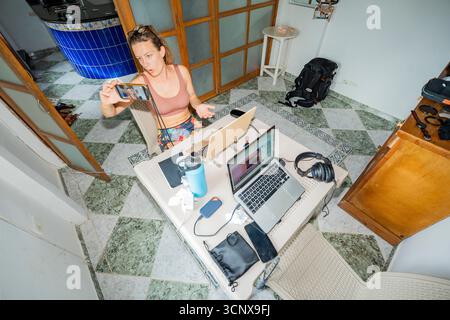 A woman embraces the digital nomad lifestyle, working from her home office. Surrounded by laptops and tech gear, she participates in a virtual meeting Stock Photo