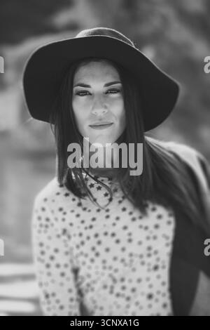 Black and white image of a woman wearing a wide-brimmed hat, with long hair and a patterned sweater, conveying elegance and timeless fashion in natura Stock Photo