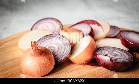Playful arrangement of red and yellow onion parts, slices, and skins on wooden cutting board. Conceptual still life with natural textures and artistic Stock Photo