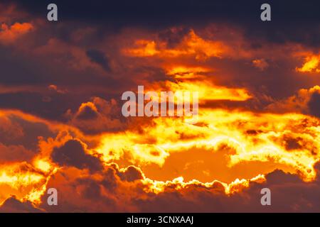 Intense golden and orange light bursts through dark dramatic clouds Stock Photo