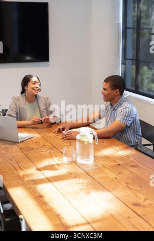 African american colleagues sitting at conference table discussing project with laptop, pitcher Stock Photo