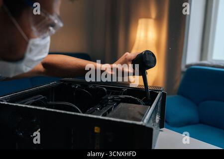 Close-up of technician in face mask and safety glasses cleaning computer case using small vacuum cleaner, demonstrating proper maintenance procedures. Stock Photo