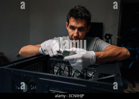 Portrait of technician male wearing protective white gloves inserting central processing unit into desktop motherboard socket during computer hardware Stock Photo