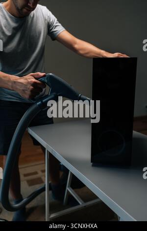 Vertical shot of technician male using vacuum cleaner to remove dust and debris from ventilation holes of computer case, performing important Stock Photo