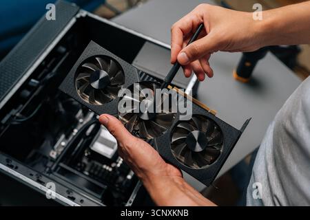Technician cleaning graphics card with brush, performing essential maintenance on computer hardware to ensure optimal performance. Stock Photo