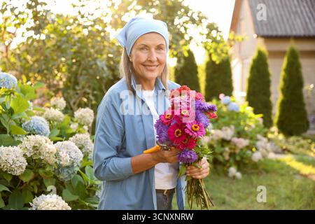 Senior woman with bouquet of flowers and pruner in garden Stock Photo