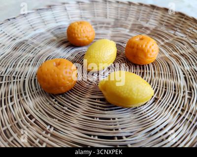 Multi-colored marzipan candies in shape of two lemon and three orange  are neatly arranged on beige wicker straw dish. Flat lay. Side view. Selective Stock Photo