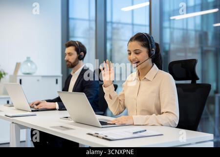Diverse customer service representatives providing online assistance and communicating with clients via video calls and headsets from a contemporary office environment Stock Photo