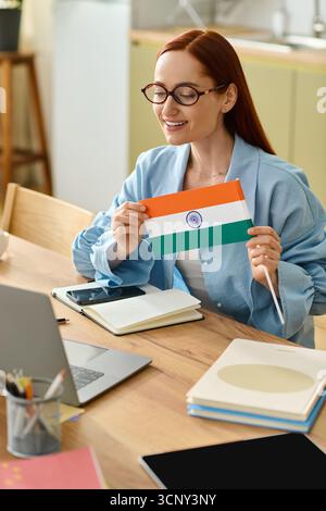 A woman with red hair teaches languages online while holding an Indian flag in her home. Stock Photo