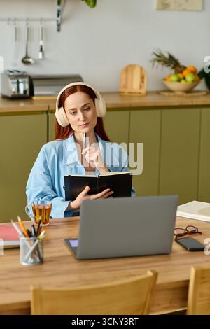 A woman with red hair teaches language online, focused on her laptop in a cozy home setting. Stock Photo