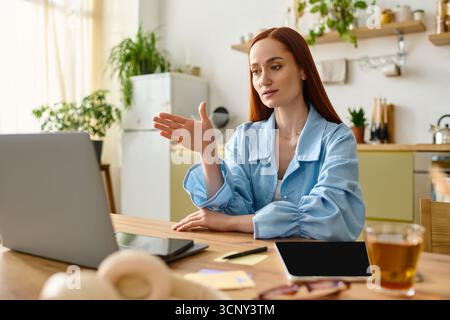 A woman with red hair teaches a language lesson online from her home, using a laptop. Stock Photo
