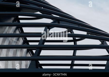 Close-up of a black metal architectural structure. The interlocking curved and straight bars create a dynamic geometric pattern against a pale blue sk Stock Photo