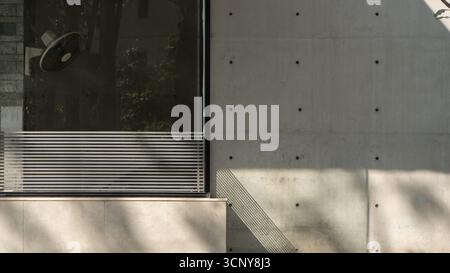 A minimalist architectural detail shot of a modern building's facade, featuring a concrete wall with dot patterns, a large window with horizontal Stock Photo