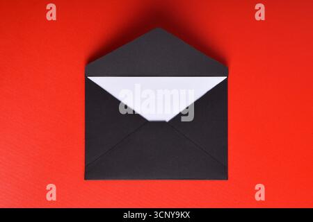 Opened black paper envelope with paper sheet isolated on red background Stock Photo