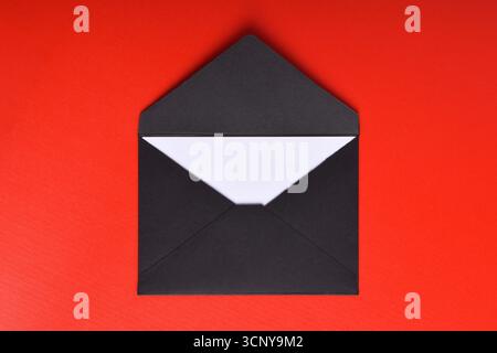 Opened black paper envelope with paper sheet isolated on red background Stock Photo