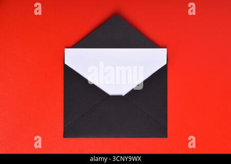 Opened black paper envelope with paper sheet isolated on red background Stock Photo
