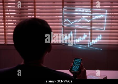 A person viewed from behind, using a phone to project a holographic stock chart. A concept for fintech, data visualization, investment strategy, virtu Stock Photo