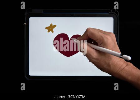 Hand drawing a red heart and yellow star on a digital tablet using a white stylus, concept of creativity, design, and modern technology. Stock Photo