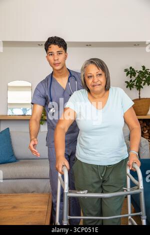 Senior hispanic woman using walker, hispanic male caregiver holding stethoscope at home Stock Photo