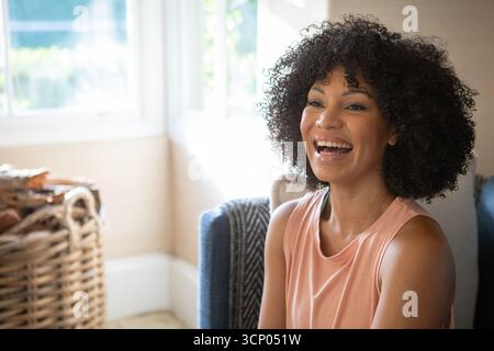 African american woman laughing on sofa by large window with wicker basket, copy space Stock Photo