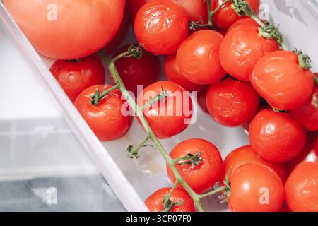 Fresh ripe cherry tomatoes on vine in plastic container. Natural organic vegetable harvest. Red tomatoes closeup. Healthy food for cooking and salad. Stock Photo