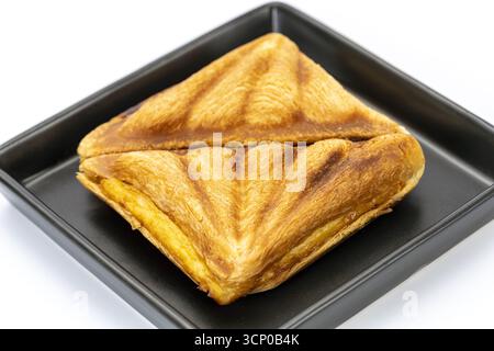 Close up of toasted triangle sandwich with melted cheese filling on black square plate, golden brown crispy bread, simple breakfast or snack food phot Stock Photo