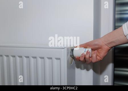 A person is adjusting a smart thermostat on a radiator to control room temperature during winter. Stock Photo