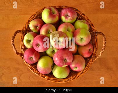 Top view of fresh red and green apples fruits in a wicker basket on a wooden table. Stock Photo