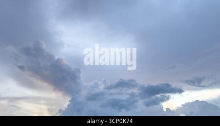 Dark gray and white clouds fill the sky as the sun sets, creating a peaceful yet dramatic atmosphere at dusk. Stock Photo