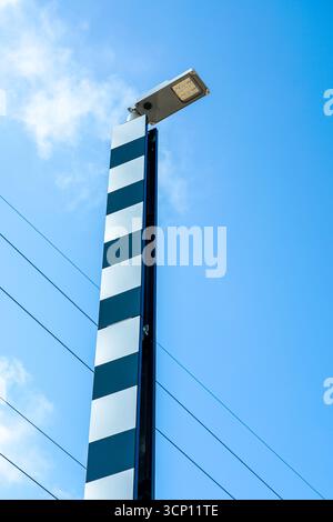 Modern LED street light with vertical black and white reflective panels against a clear blue sky and power lines background Stock Photo