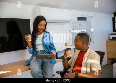 African American male colleagues holding coffee cups and tablet sitting, discussing at office desk Stock Photo