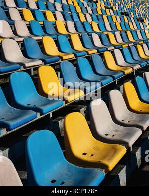 Empty stadium - dirty tribune seats. Rows of yellow, blue and off-white seats in a stadium Stock Photo