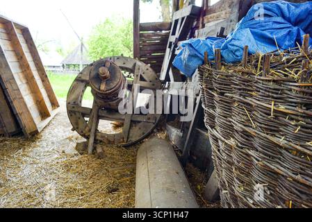 A barn in a village: view of hay scattered on the floor, an old wheel, a wicker basket. Rural lifestyle, eco-friendly living, agritourism experiences Stock Photo