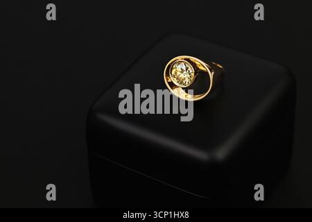 A gold ring with a diamond in the center sits on a black background. The ring is the main focus of the image, and the black background emphasizes its Stock Photo