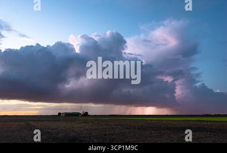 Stormy sky over open farm field at sunset with heavy clouds and distant horizon. Stock Photo