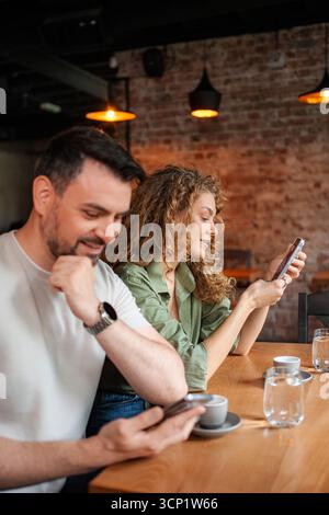 Young couple using smartphones in a cafe, ignoring each other Stock Photo
