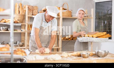 Senior man works in bakery as baker, kneads dough, works with flour. Stock Photo