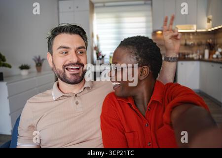 Happy multi-ethnic couple taking a selfie on the sofa at home Stock Photo