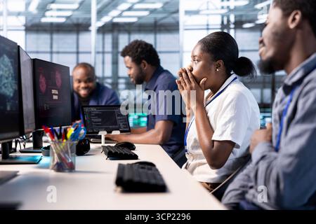 Engineer in server farm frightened by hacker passing firewall and stealing data. Security breach notification on monitor in data center scaring woman, requesting help from colleagues Stock Photo