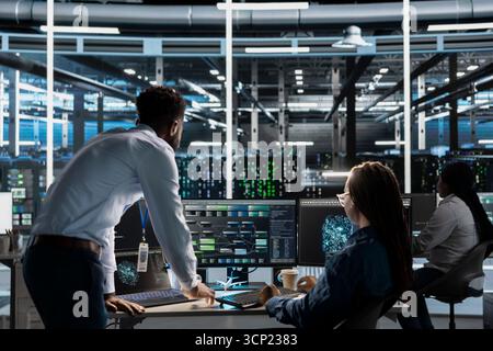 Data center manager supervises engineer using AI visual programming to optimize gear. Server farm team leader overseeing work done by worker colleagues using artificial intelligence analysis software Stock Photo