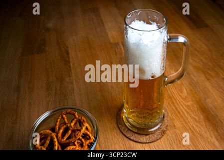 beer in a traditional beer mug with a head of foam on a wooden table with mini beer pretzels in a glass vase close-up selective focus Stock Photo